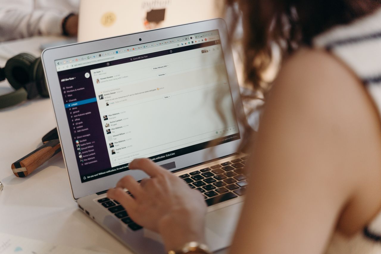 Home A businesswoman typing on a laptop in an office setting, using Slack for communication.